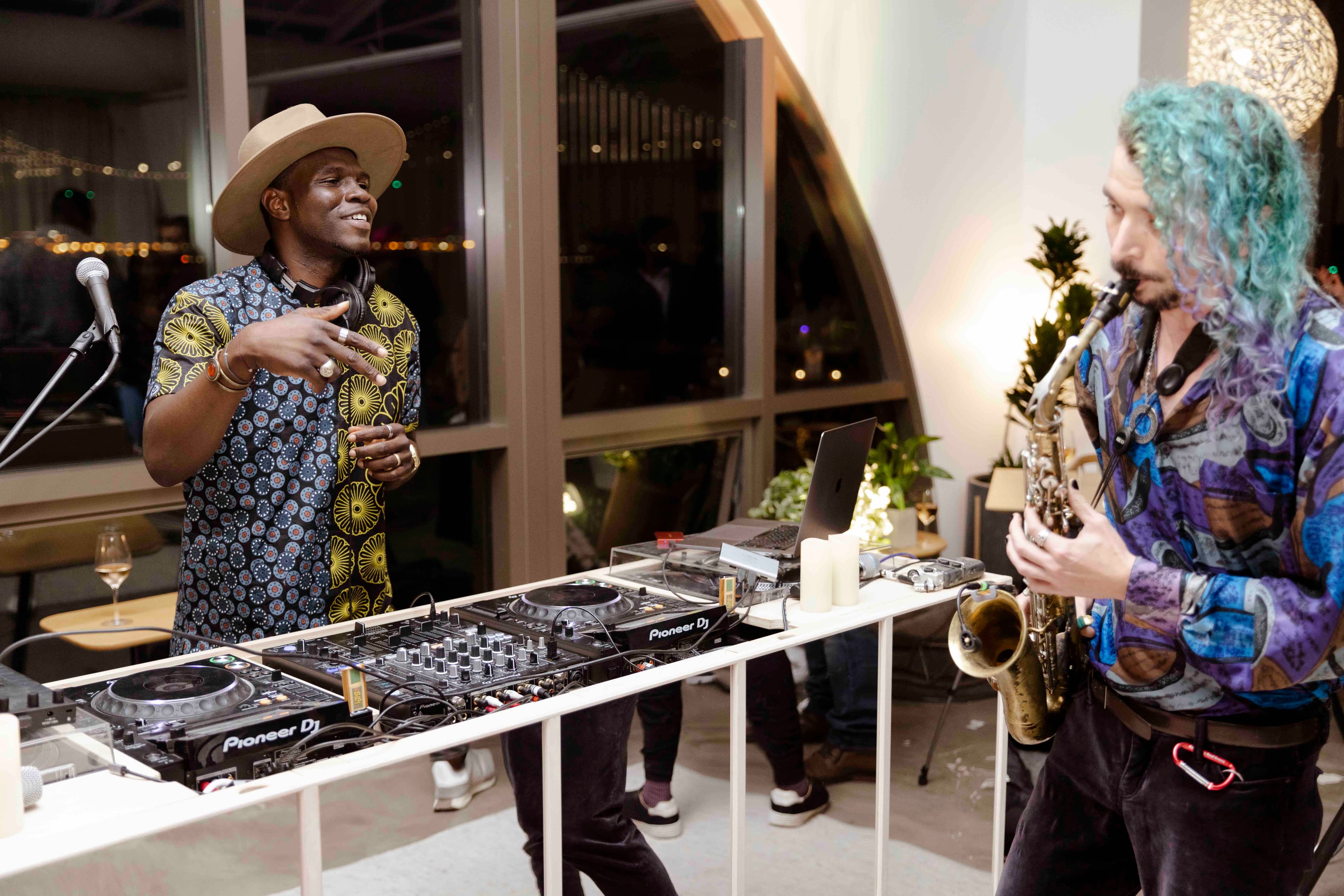 Bisi DJing alongside a live saxophonist at an evening event