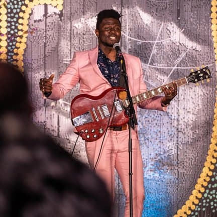 Bisi performing in a pink suit with an electric guitar